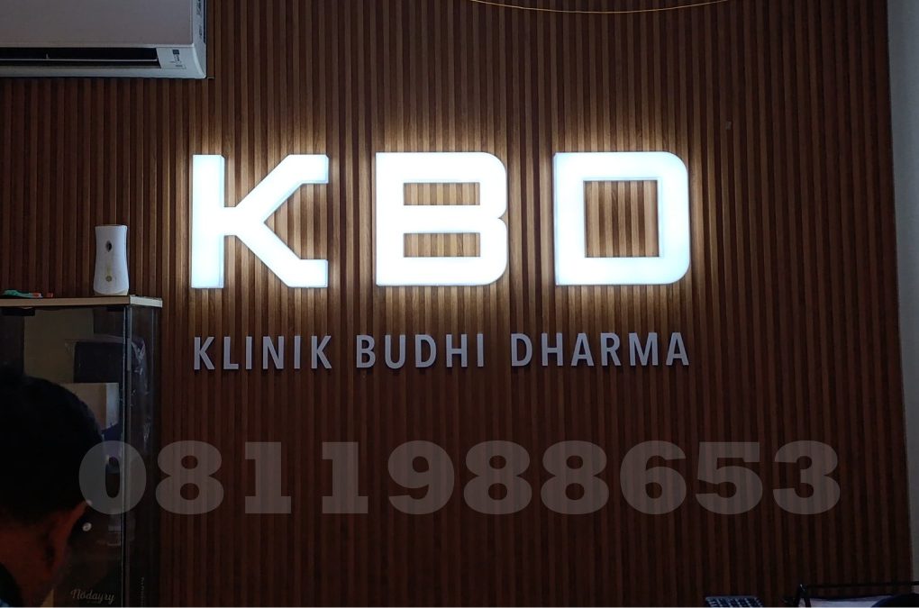 Huruf timbul akrilik LED KBD Klinik Budhi Dharma dengan efek backlit putih elegan di dinding kayu interior