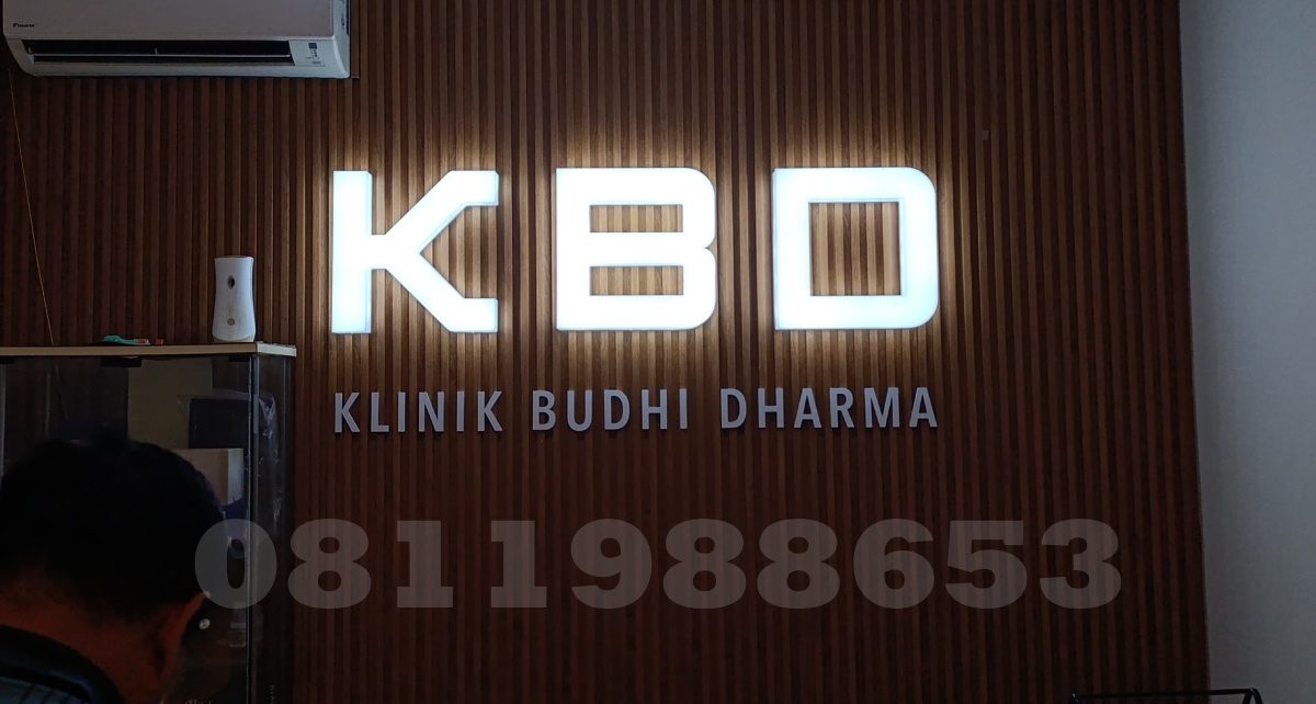 Huruf timbul akrilik LED KBD Klinik Budhi Dharma dengan efek backlit putih elegan di dinding kayu interior