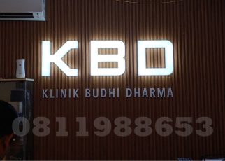 Huruf timbul akrilik LED KBD Klinik Budhi Dharma dengan efek backlit putih elegan di dinding kayu interior